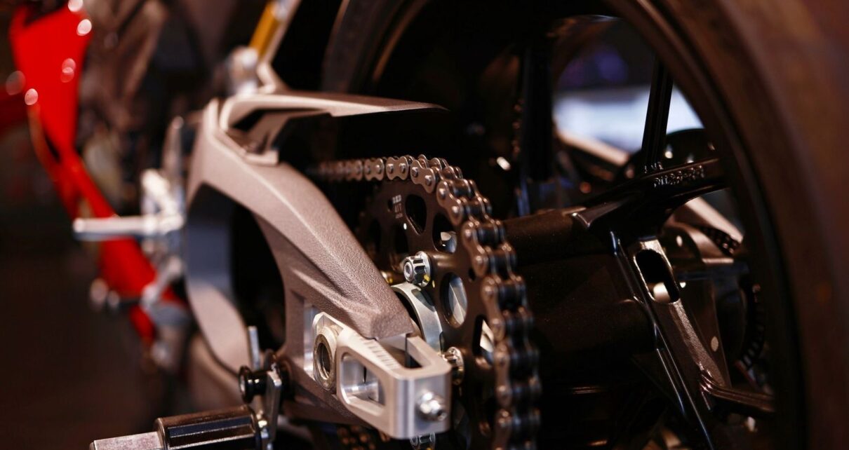 Close-up of a motorcycle rear sprocket, chain, axle, and swingarm